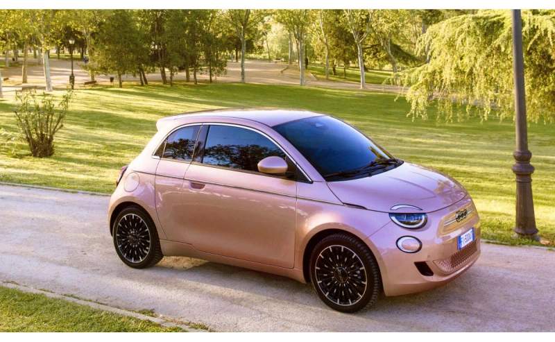 Fiat 500e w kolorze różowym, zaparkowany w parku miejskim
